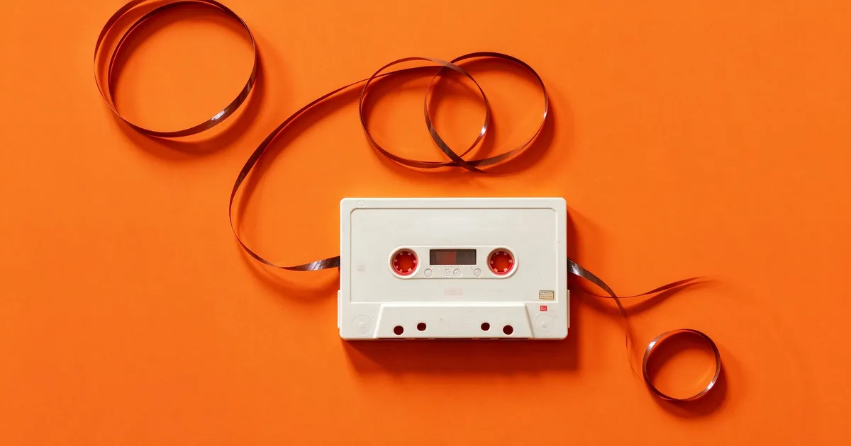 White cassette tape with its magnetic ribbon unspooled on an orange background